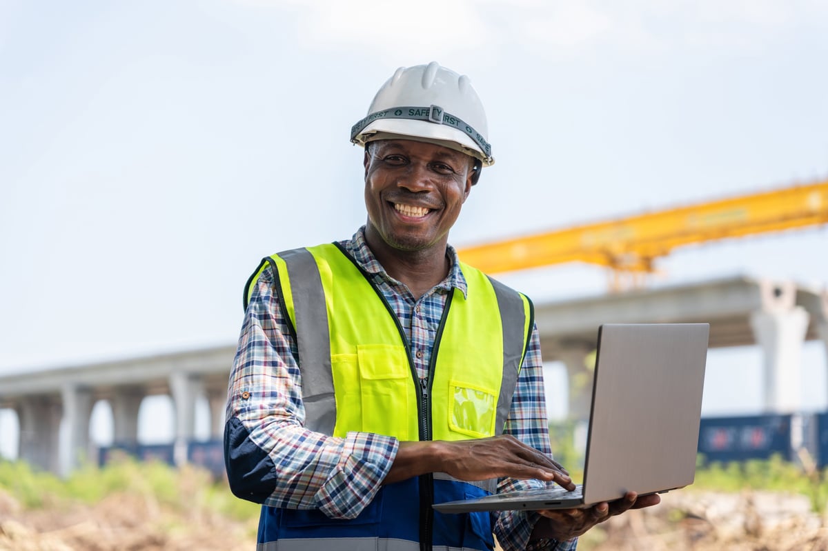 Smiling African American construction engineer working on a laptop at a project site